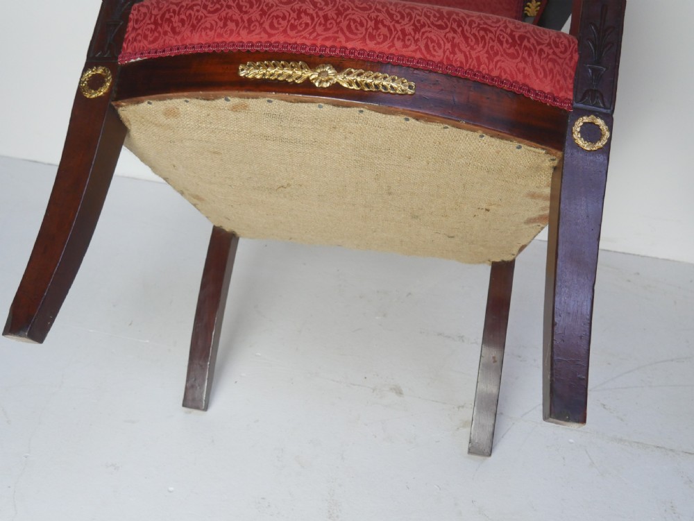 A French Empire style mahogany armchair featuring red damask fabric upholstery, carved armrests, and decorative gilded bronze mounts. View XIII