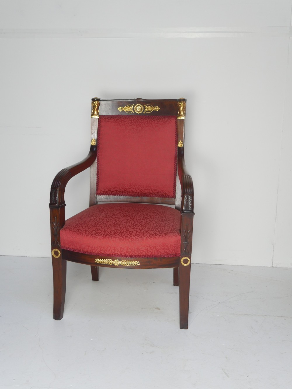 A French Empire style mahogany armchair featuring red damask fabric upholstery, carved armrests, and decorative gilded bronze mounts. View XIV