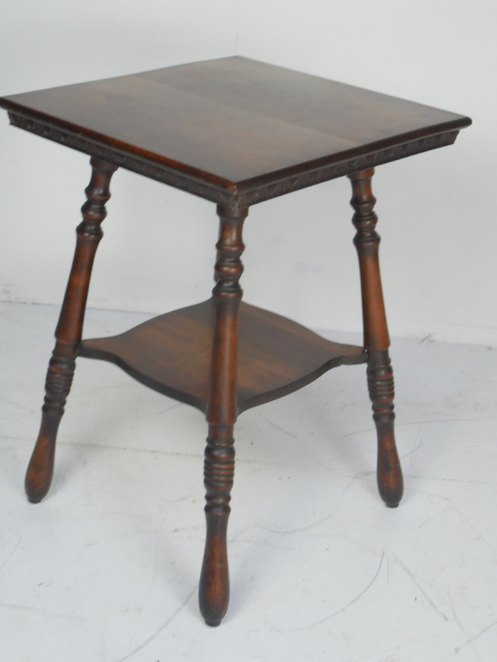 A dark brown wooden 1920s lamp table featuring four turned legs, a square top with carved edge detailing, and a lower tier shelf. View VIII