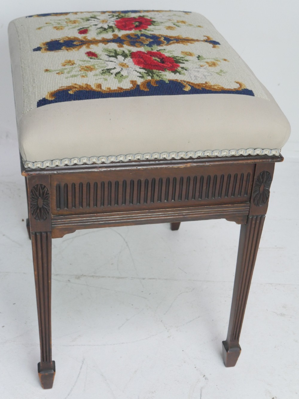 A rectangular antique mahogany piano stool featuring fluted tapered legs, carved central rosettes, and a floral needlepoint tapestry top. View VII