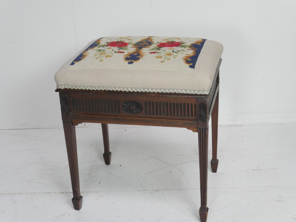 A rectangular antique mahogany piano stool featuring fluted tapered legs, carved central rosettes, and a floral needlepoint tapestry top. View XII
