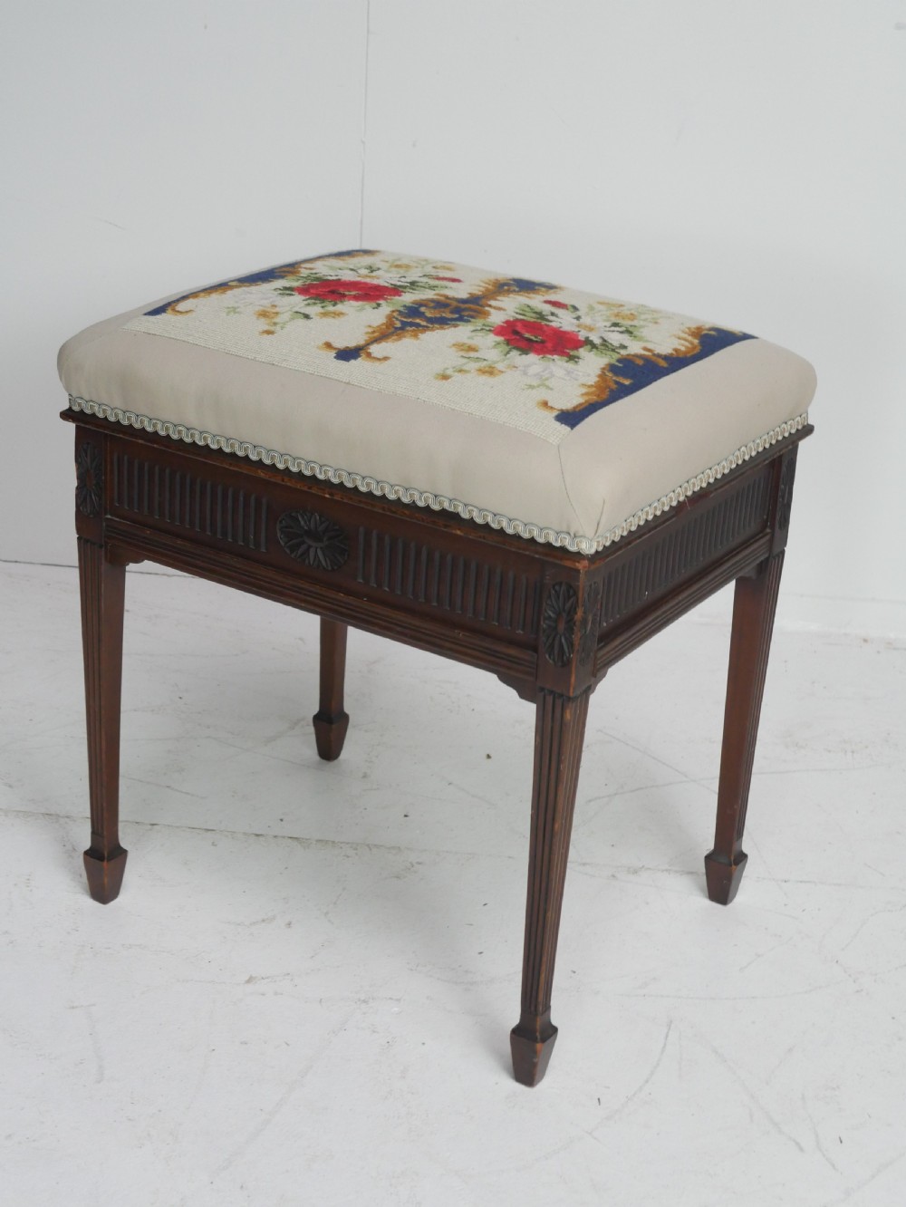 A rectangular antique mahogany piano stool featuring fluted tapered legs, carved central rosettes, and a floral needlepoint tapestry top. View XIV