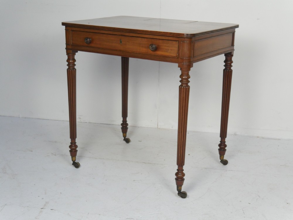 A Regency mahogany chamber writing desk featuring reeded turned legs, a single frieze drawer, and brass castors.