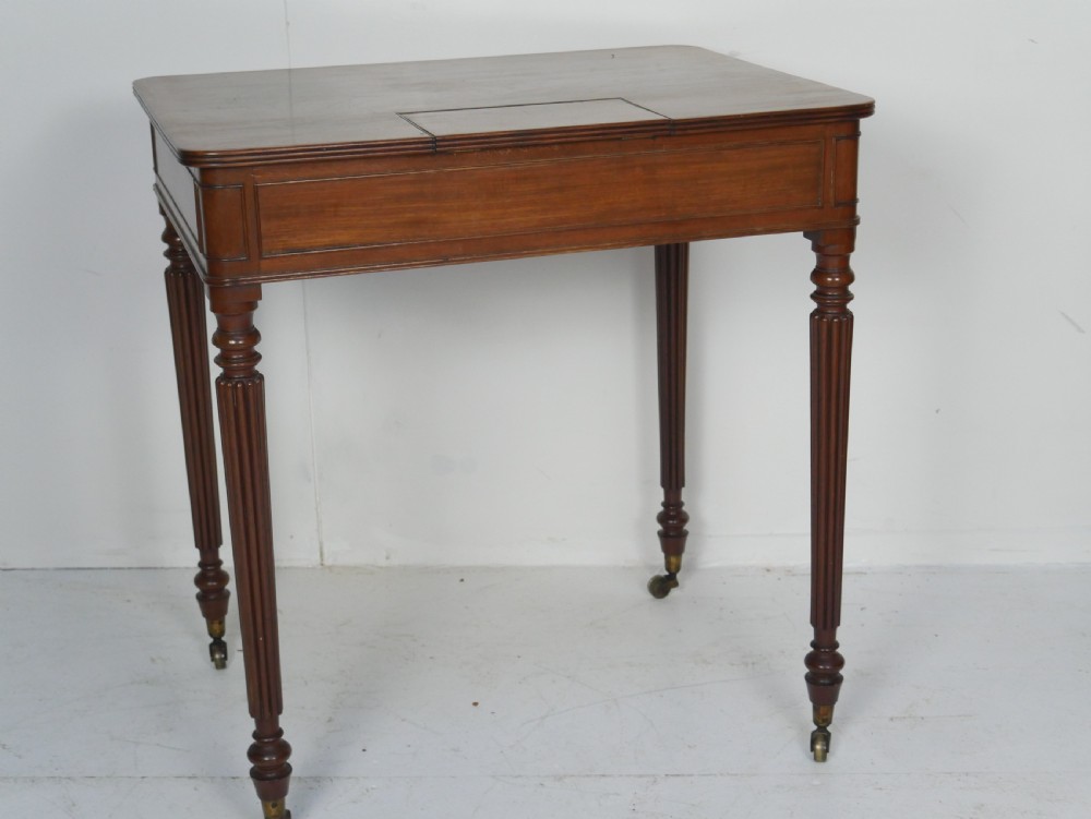 A Regency mahogany chamber writing desk featuring reeded turned legs, a single frieze drawer, and brass castors. View V