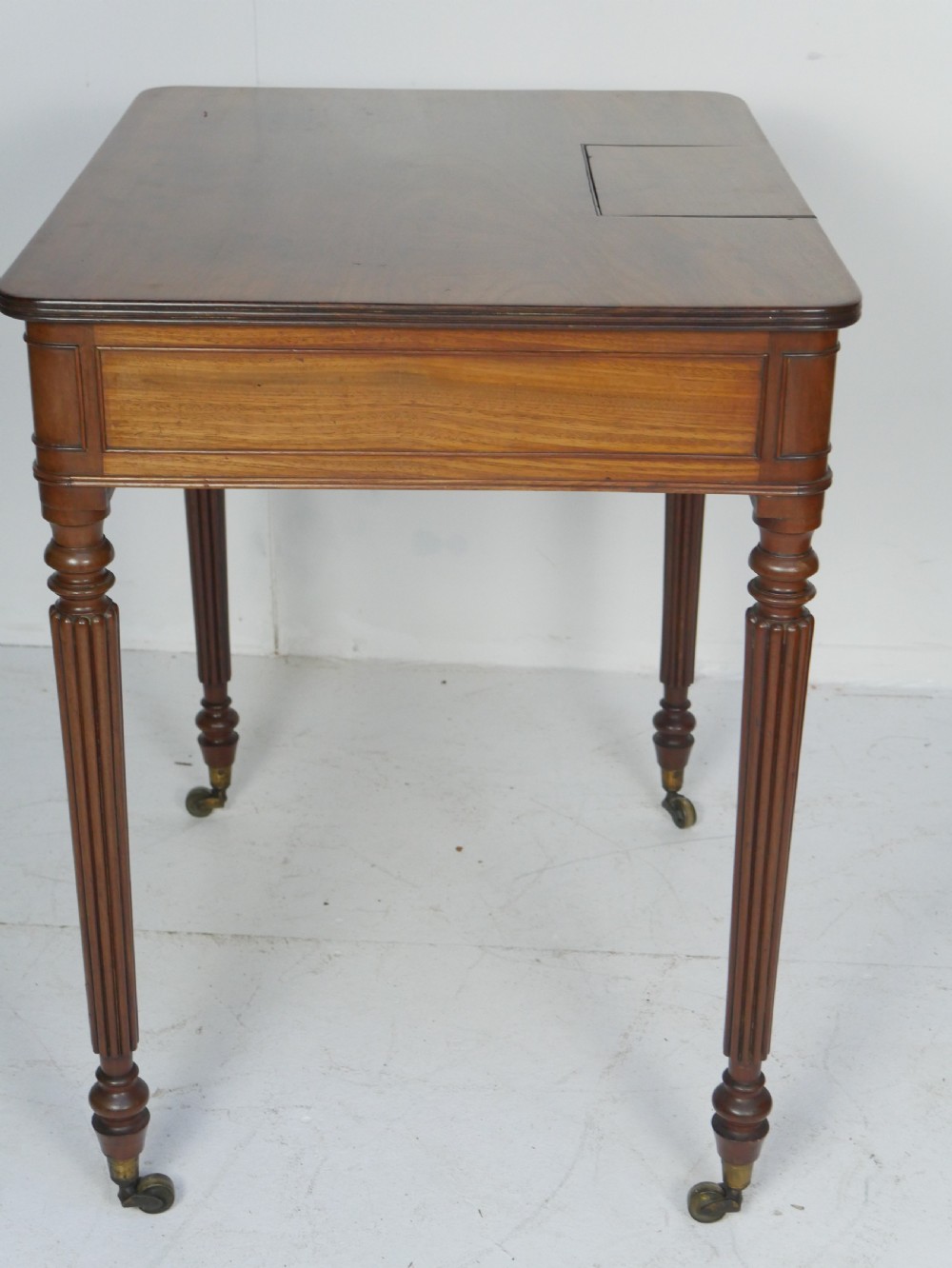 A Regency mahogany chamber writing desk featuring reeded turned legs, a single frieze drawer, and brass castors. View VI