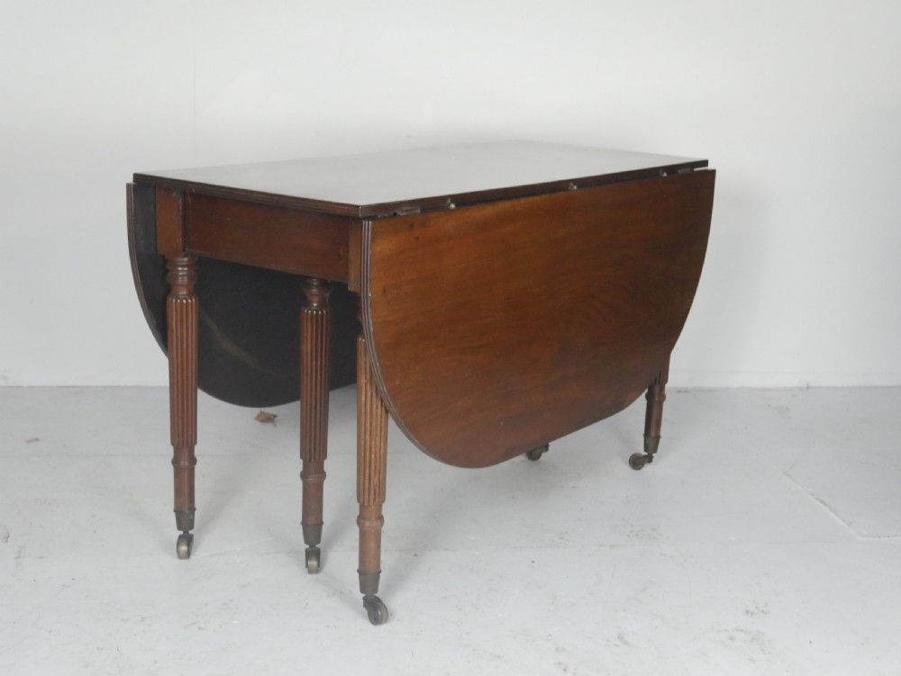 An antique mahogany drop-leaf dining table with reeded legs set on brass castors, shown fully extended. View II