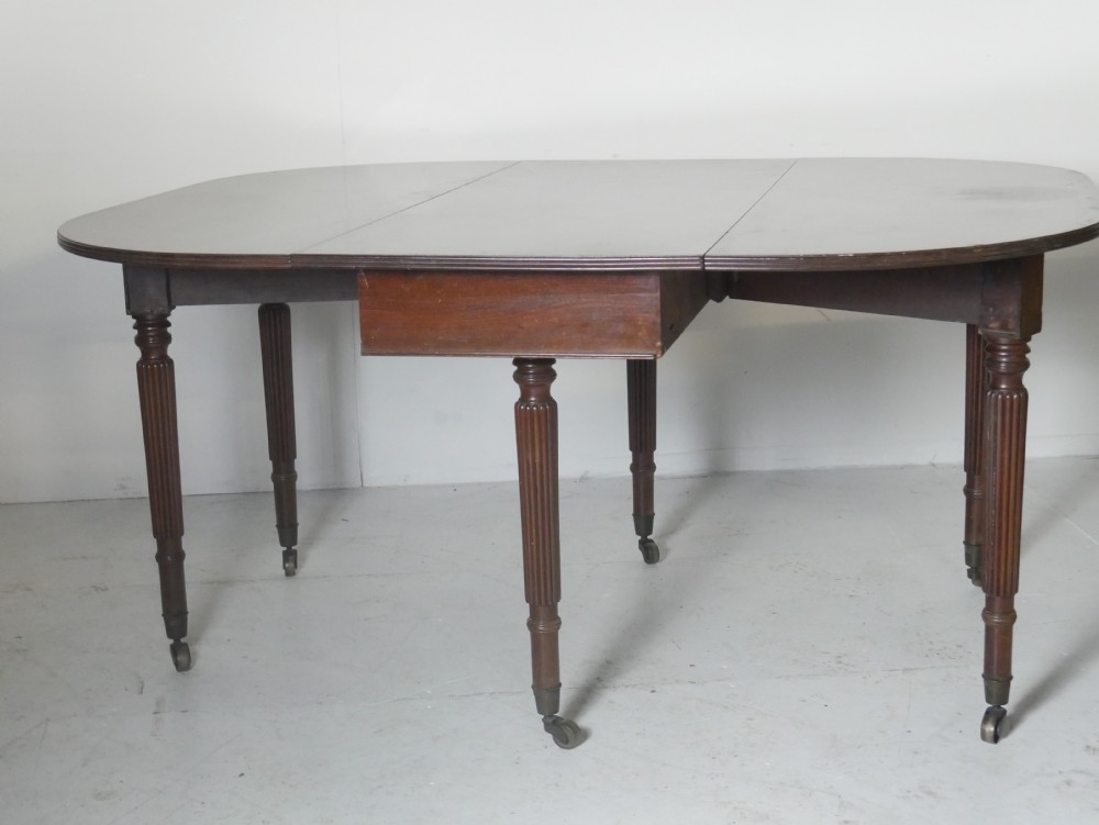 An antique mahogany drop-leaf dining table with reeded legs set on brass castors, shown fully extended.