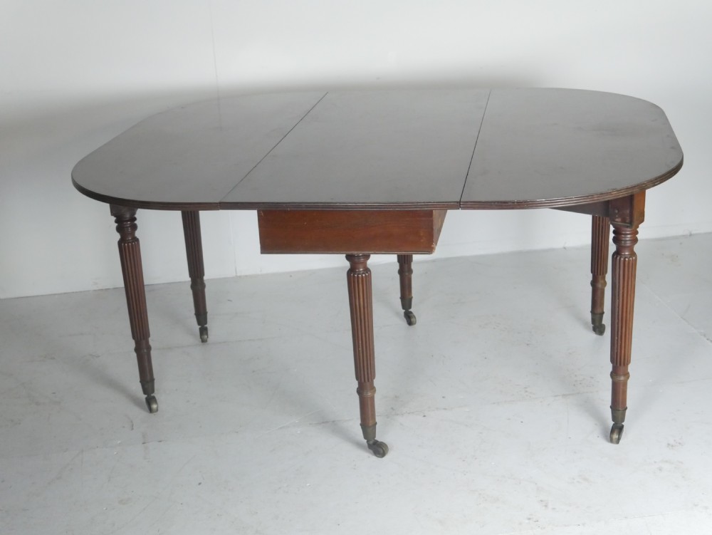 An antique mahogany drop-leaf dining table with reeded legs set on brass castors, shown fully extended. View VIII