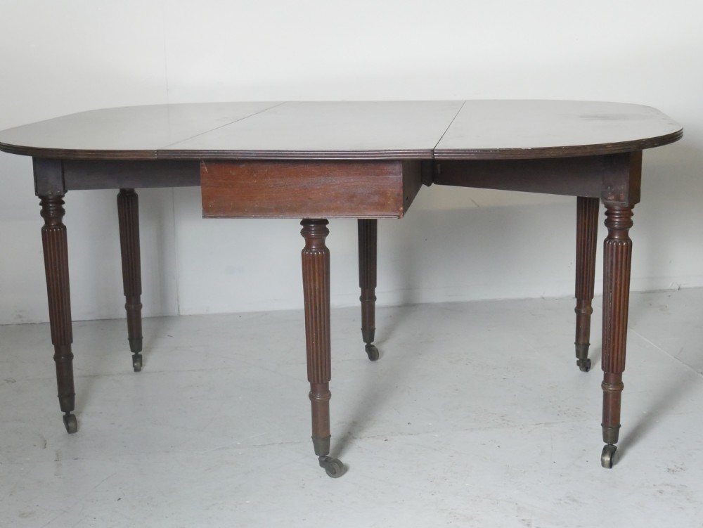 An antique mahogany drop-leaf dining table with reeded legs set on brass castors, shown fully extended. View X