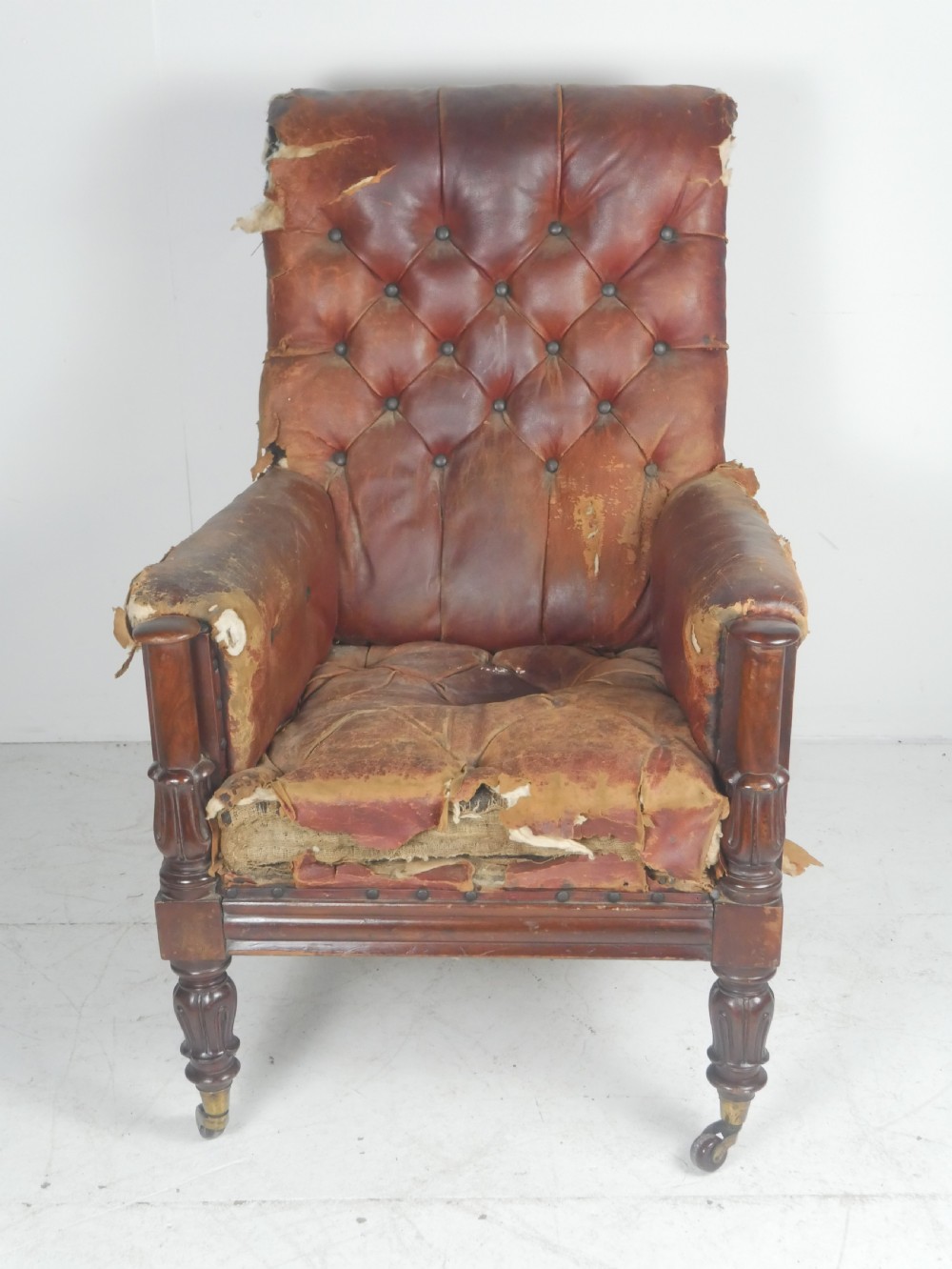 A distressed Regency library armchair with deep-buttoned red leather upholstery, turned mahogany front legs, and brass castors. View II