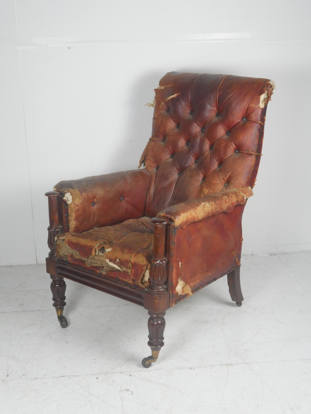 A distressed Regency library armchair with deep-buttoned red leather upholstery, turned mahogany front legs, and brass castors. View III