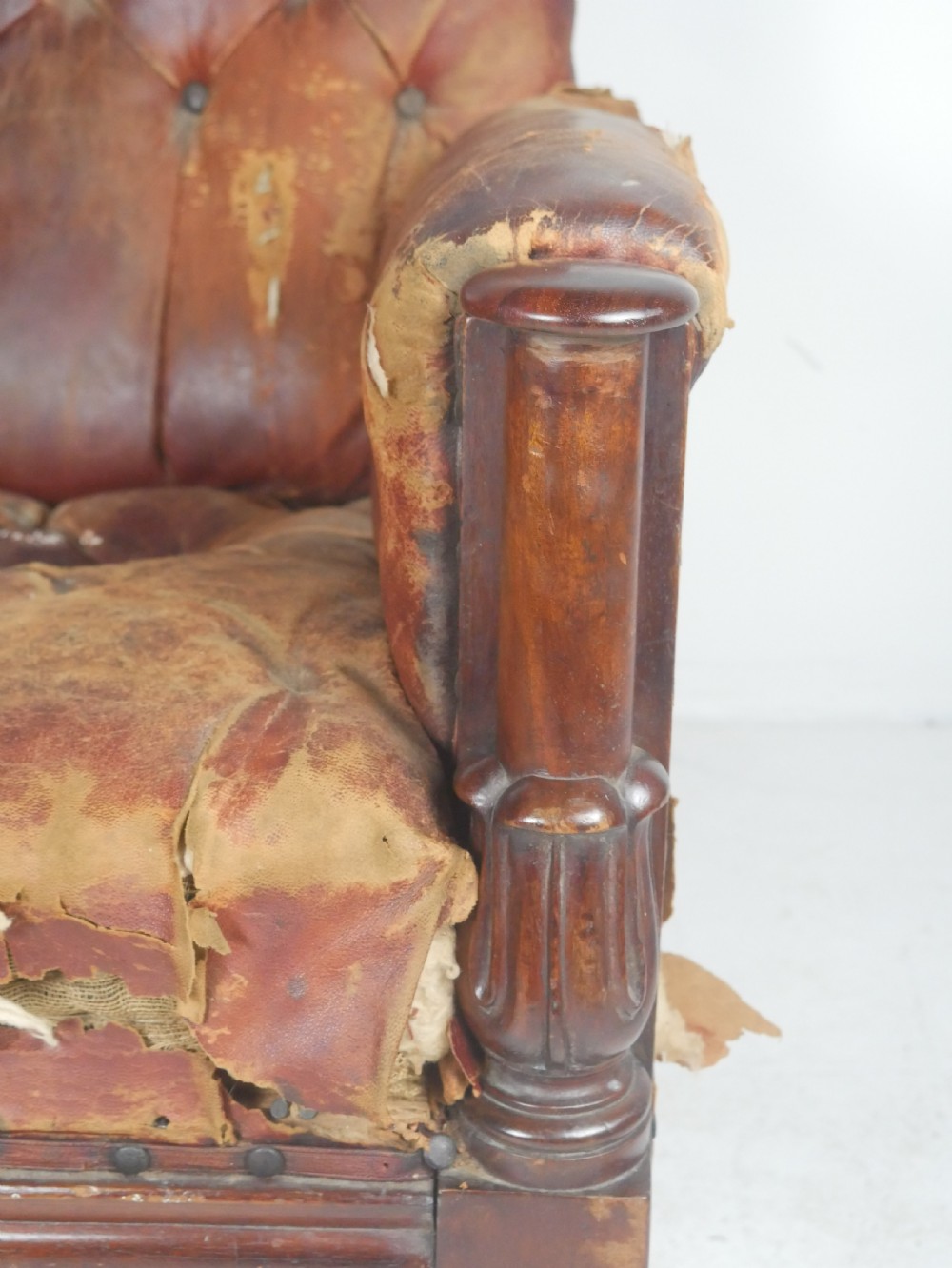 A distressed Regency library armchair with deep-buttoned red leather upholstery, turned mahogany front legs, and brass castors. View V