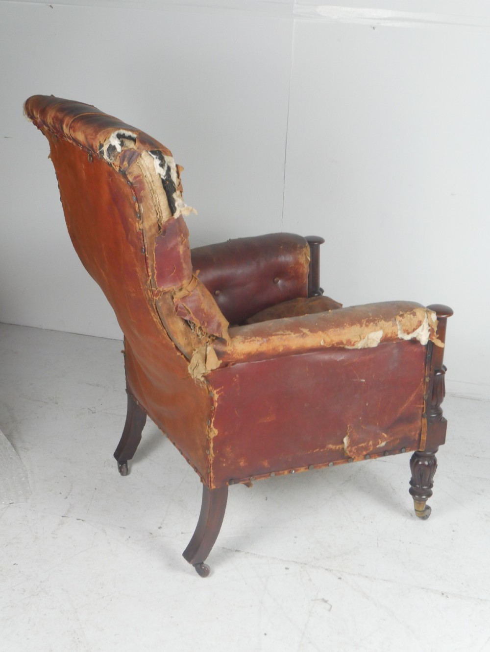 A distressed Regency library armchair with deep-buttoned red leather upholstery, turned mahogany front legs, and brass castors. View XI