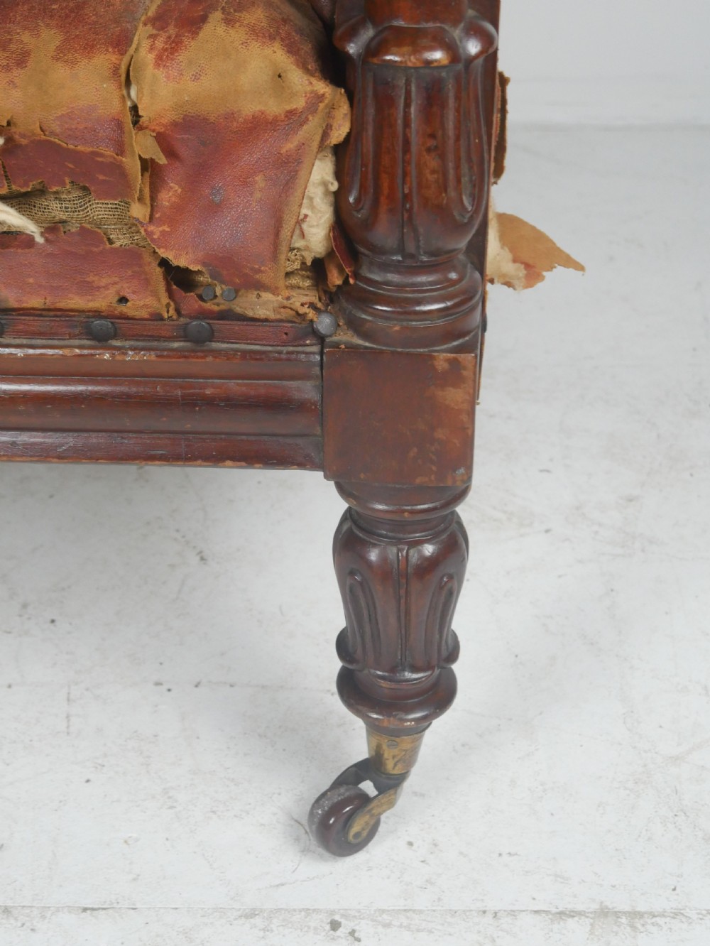 A distressed Regency library armchair with deep-buttoned red leather upholstery, turned mahogany front legs, and brass castors. View XII