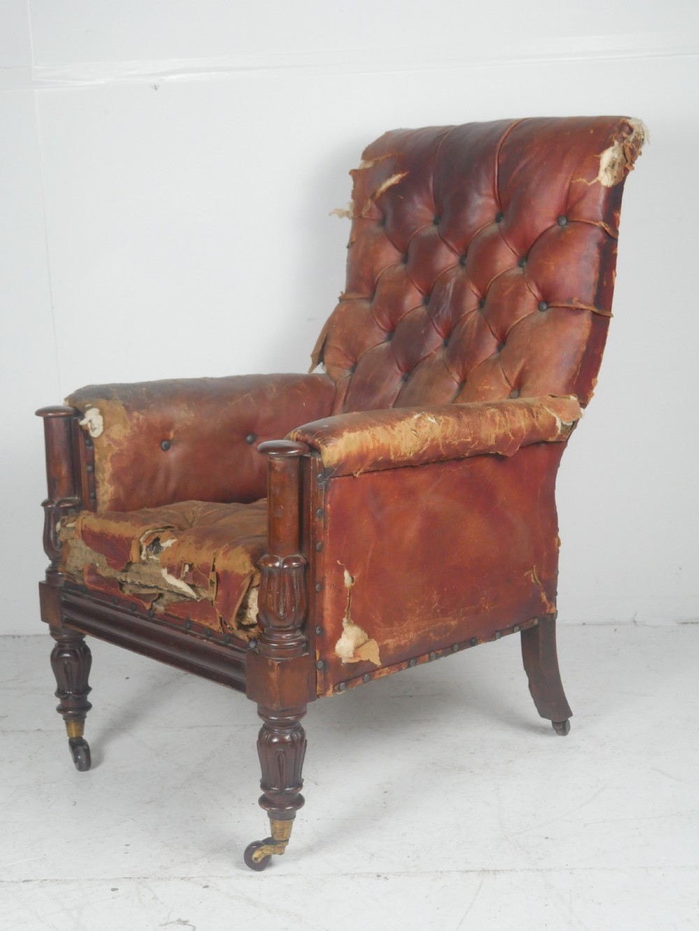 A distressed Regency library armchair with deep-buttoned red leather upholstery, turned mahogany front legs, and brass castors. View XIII