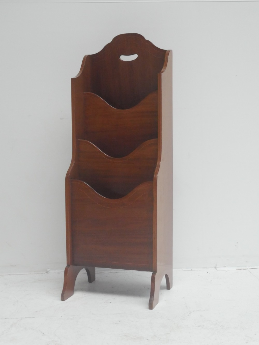 A freestanding three-tiered mahogany magazine rack featuring curved cutout fronts, an integrated top handle, and inlaid stringing borders on splayed feet. View VIII