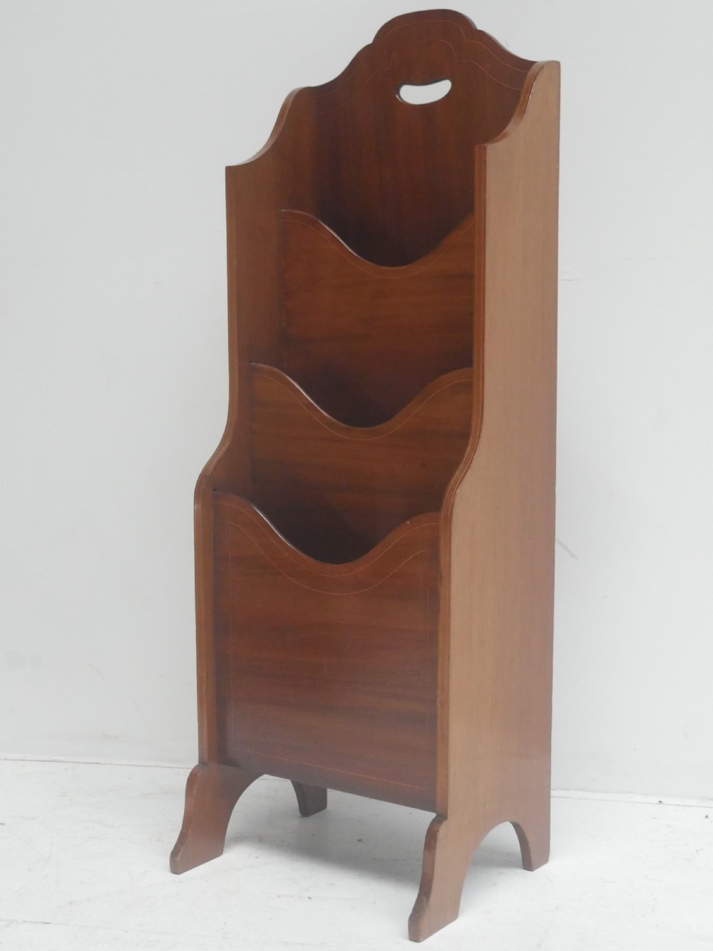 A freestanding three-tiered mahogany magazine rack featuring curved cutout fronts, an integrated top handle, and inlaid stringing borders on splayed feet. View IX