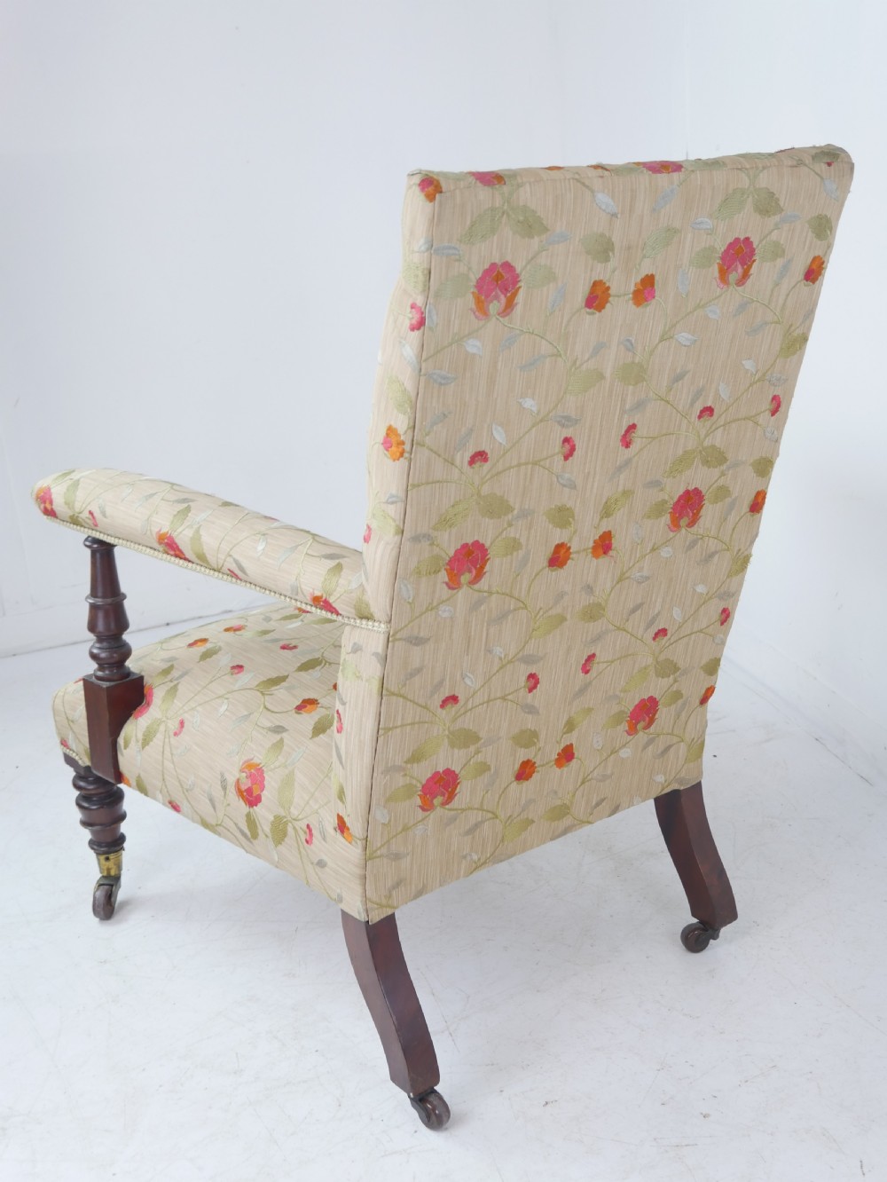 A 19th-century Victorian armchair featuring beige floral upholstery, a deep button-back rest, padded armrests, and turned mahogany legs set on brass casters. View VIII
