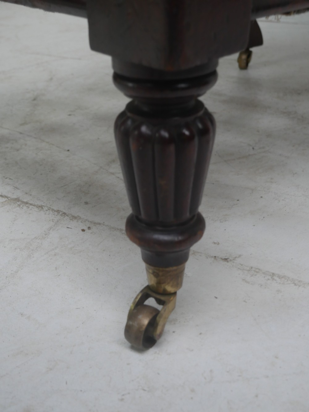 A 19th-century mahogany armchair frame featuring carved scroll arm terminals, turned front legs on brass castors, and worn calico lining ready for upholstery. View VII