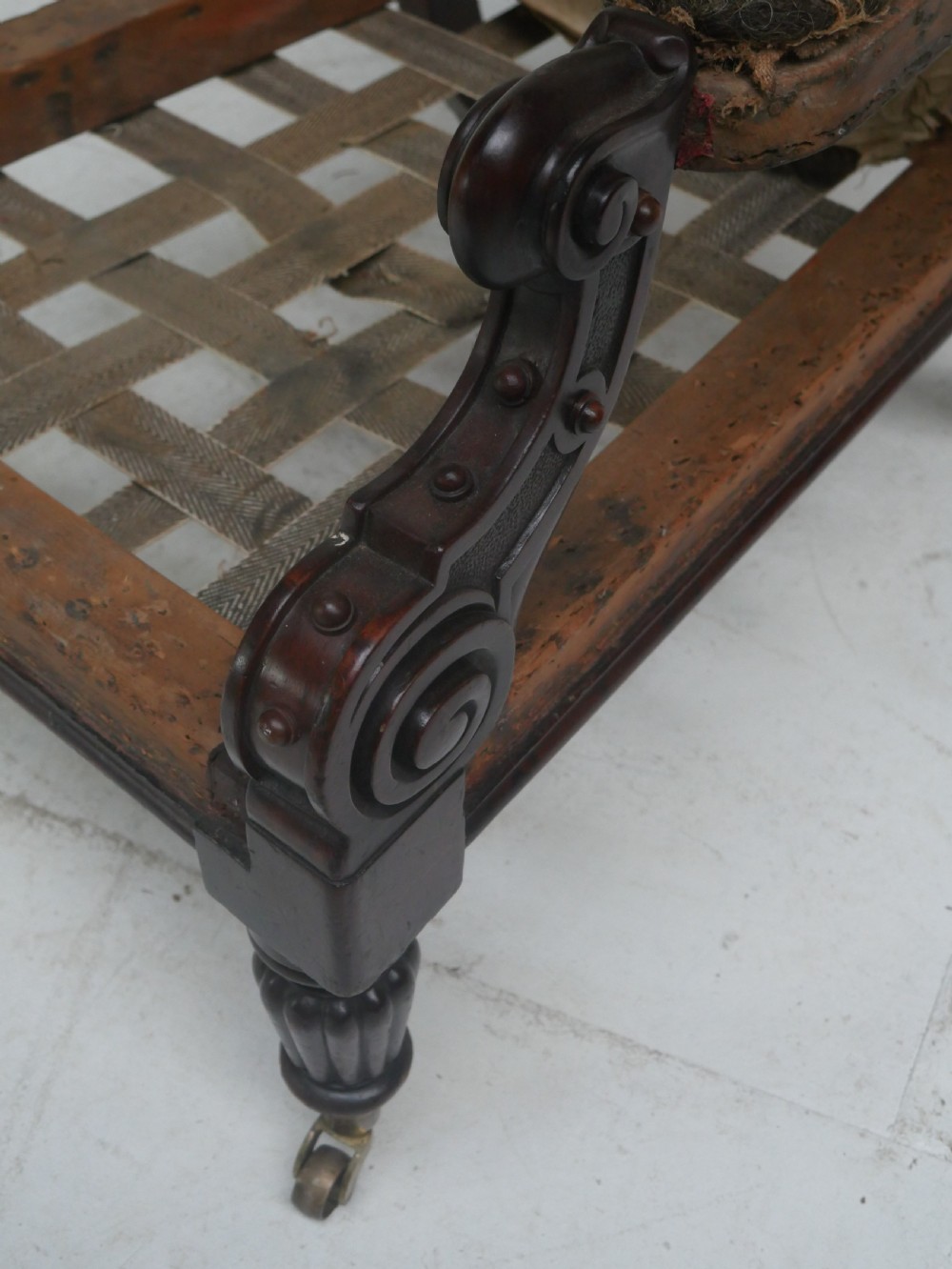 A 19th-century mahogany armchair frame featuring carved scroll arm terminals, turned front legs on brass castors, and worn calico lining ready for upholstery. View VIII