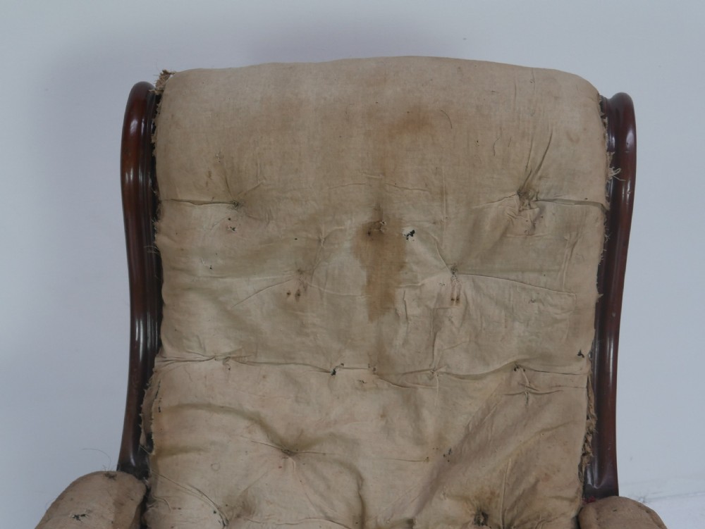 A 19th-century mahogany armchair frame featuring carved scroll arm terminals, turned front legs on brass castors, and worn calico lining ready for upholstery. View IX