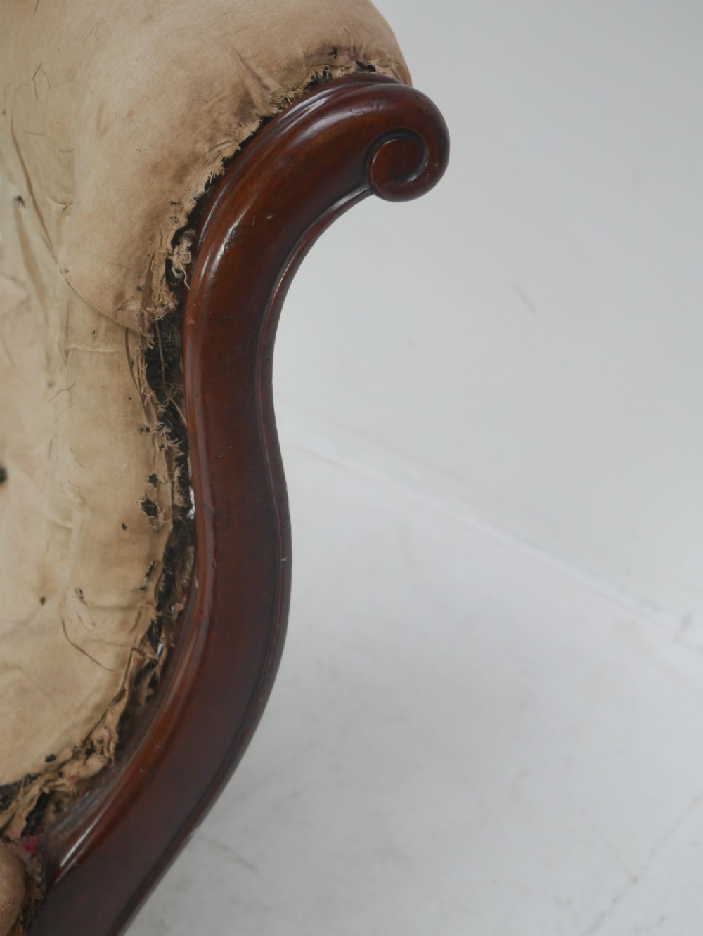 A 19th-century mahogany armchair frame featuring carved scroll arm terminals, turned front legs on brass castors, and worn calico lining ready for upholstery. View X