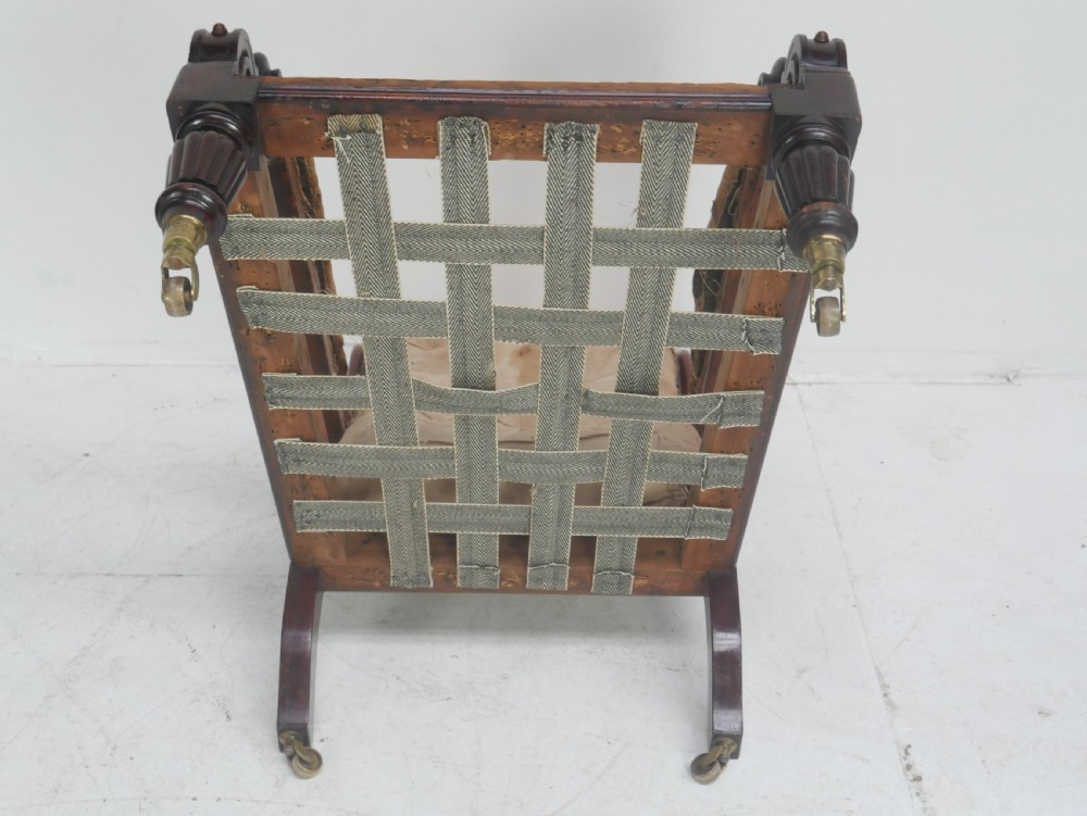 A 19th-century mahogany armchair frame featuring carved scroll arm terminals, turned front legs on brass castors, and worn calico lining ready for upholstery. View XI