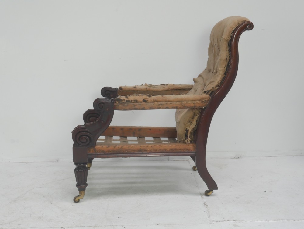 A 19th-century mahogany armchair frame featuring carved scroll arm terminals, turned front legs on brass castors, and worn calico lining ready for upholstery. View II
