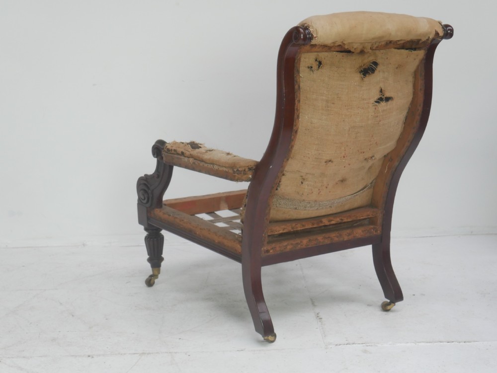 A 19th-century mahogany armchair frame featuring carved scroll arm terminals, turned front legs on brass castors, and worn calico lining ready for upholstery. View III