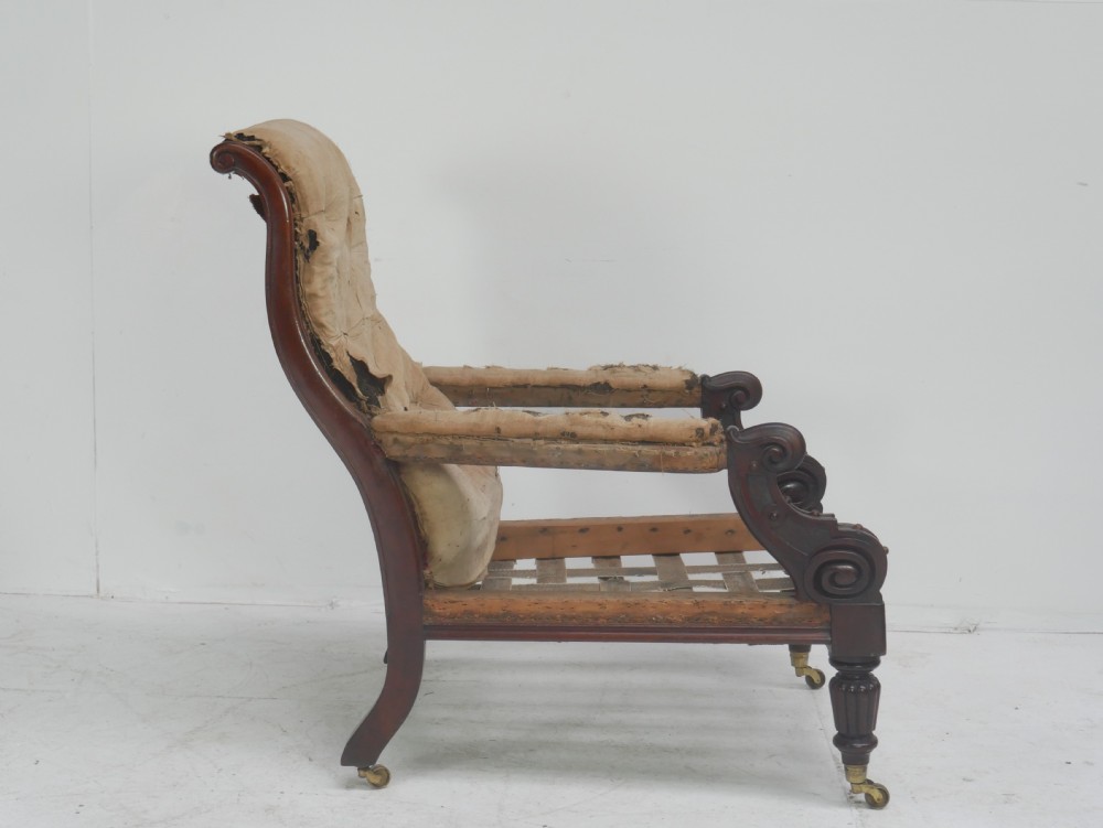 A 19th-century mahogany armchair frame featuring carved scroll arm terminals, turned front legs on brass castors, and worn calico lining ready for upholstery. View VI