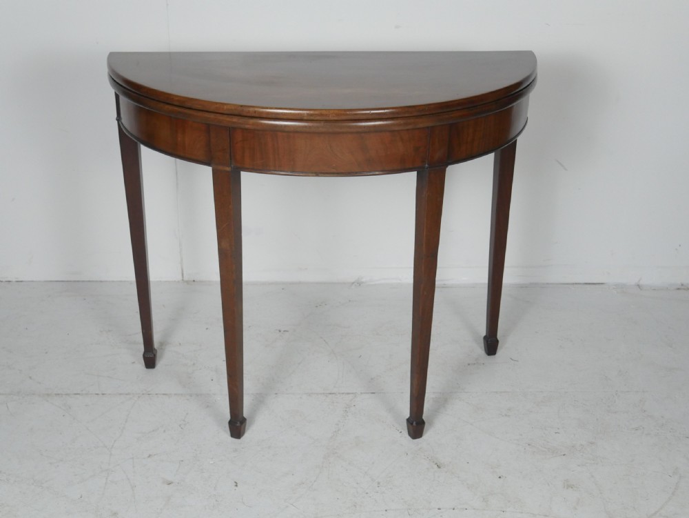 A Georgian mahogany demi-lune side table featuring a semicircular top, a plain apron, and four tapered square legs with spade feet.