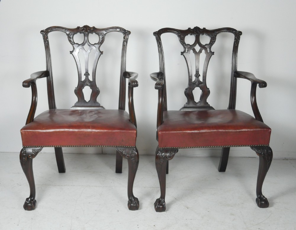 A pair of 19th-century Chippendale style mahogany armchairs featuring pierced back splats, reddish-brown leather seats with studding, and cabriole legs with ball-and-claw feet.