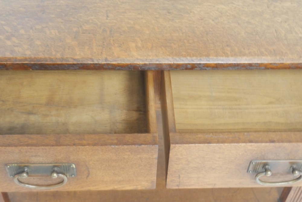 An Arts and Crafts solid oak side table featuring two drawers with brass handles, fluted legs, and a lower shelf. View III