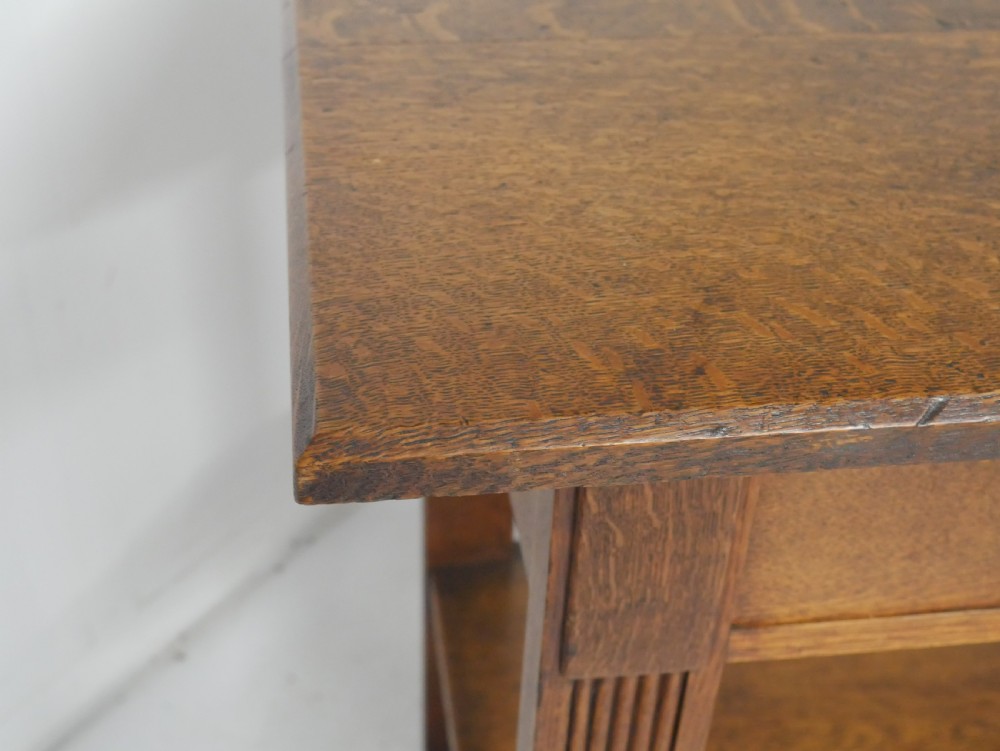 An Arts and Crafts solid oak side table featuring two drawers with brass handles, fluted legs, and a lower shelf. View VI