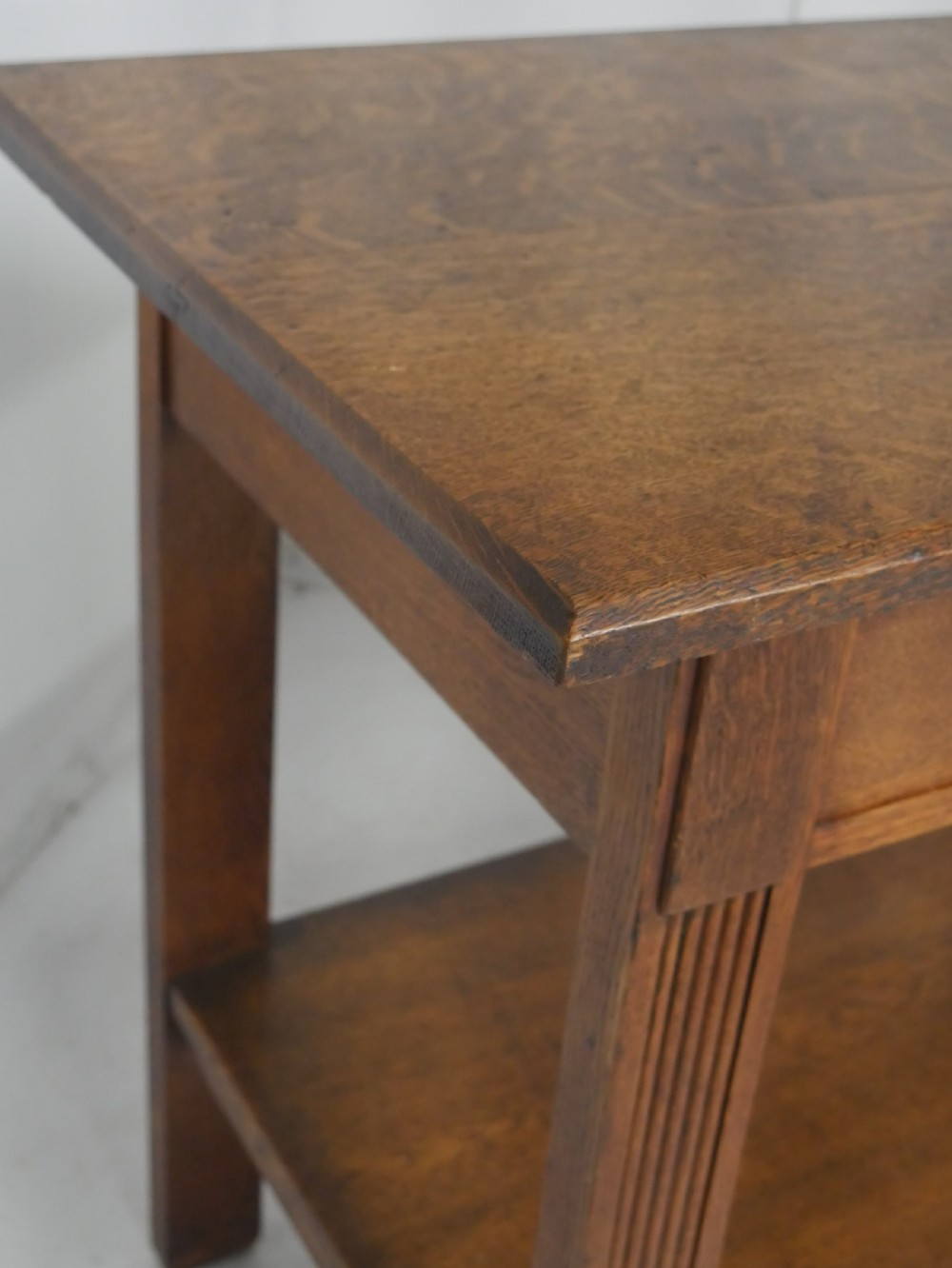 An Arts and Crafts solid oak side table featuring two drawers with brass handles, fluted legs, and a lower shelf. View VII