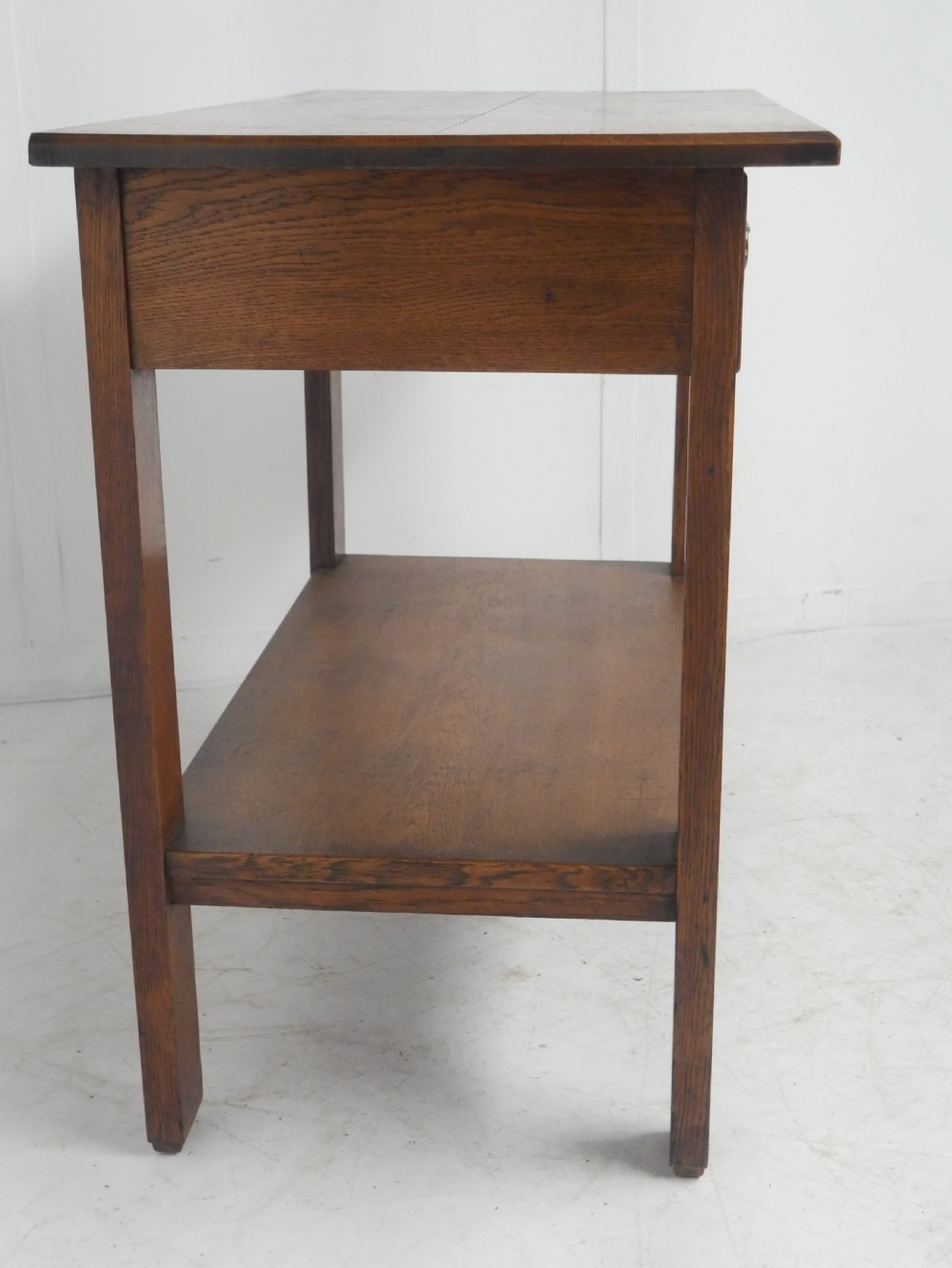 An Arts and Crafts solid oak side table featuring two drawers with brass handles, fluted legs, and a lower shelf. View VIII