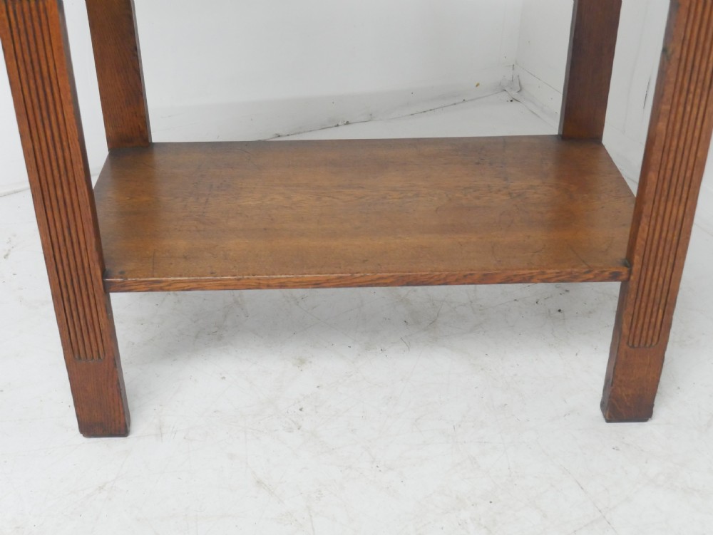 An Arts and Crafts solid oak side table featuring two drawers with brass handles, fluted legs, and a lower shelf. View IX