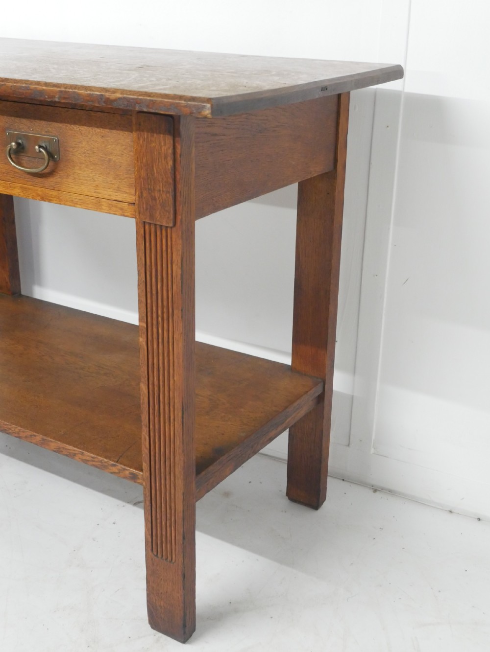An Arts and Crafts solid oak side table featuring two drawers with brass handles, fluted legs, and a lower shelf. View XI