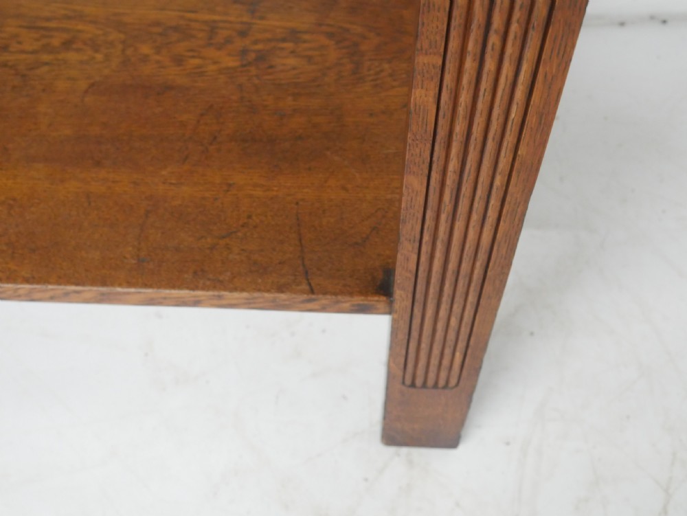 An Arts and Crafts solid oak side table featuring two drawers with brass handles, fluted legs, and a lower shelf. View XII