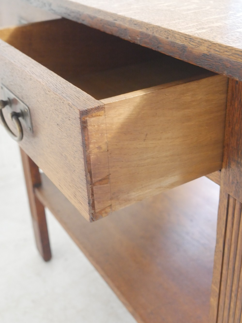 An Arts and Crafts solid oak side table featuring two drawers with brass handles, fluted legs, and a lower shelf. View XIII