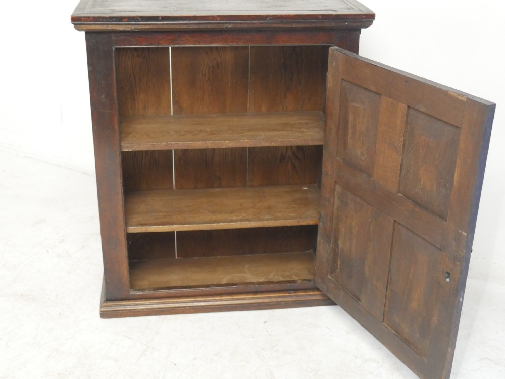 A dark brown Georgian oak wall cupboard with a single four-panel door, brass keyhole escutcheon, and moulded top cornice. View IV