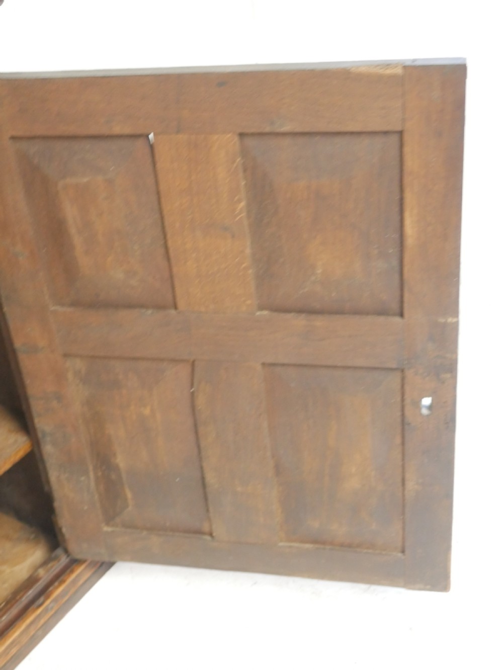 A dark brown Georgian oak wall cupboard with a single four-panel door, brass keyhole escutcheon, and moulded top cornice. View V
