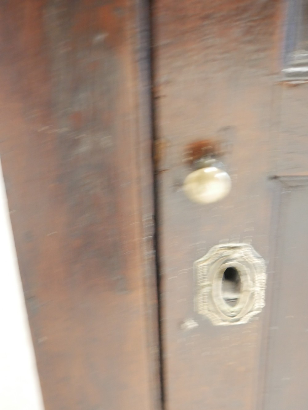 A dark brown Georgian oak wall cupboard with a single four-panel door, brass keyhole escutcheon, and moulded top cornice. View IX