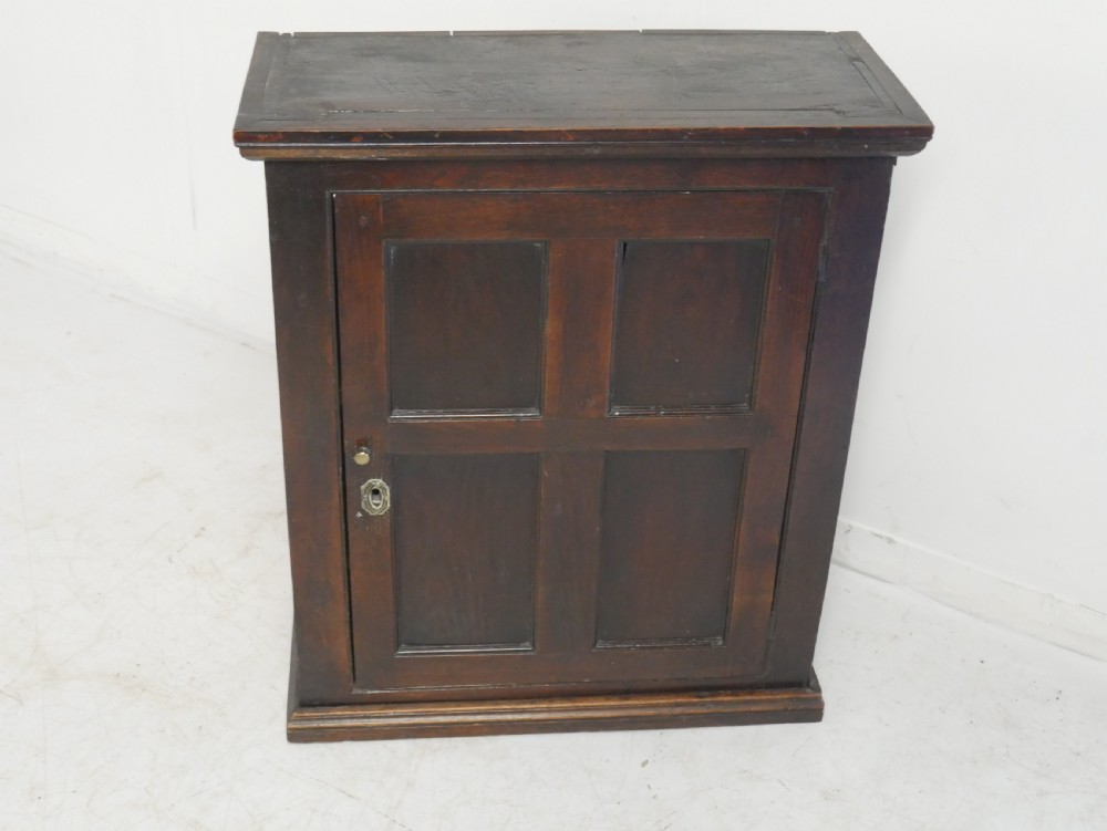 A dark brown Georgian oak wall cupboard with a single four-panel door, brass keyhole escutcheon, and moulded top cornice. View X