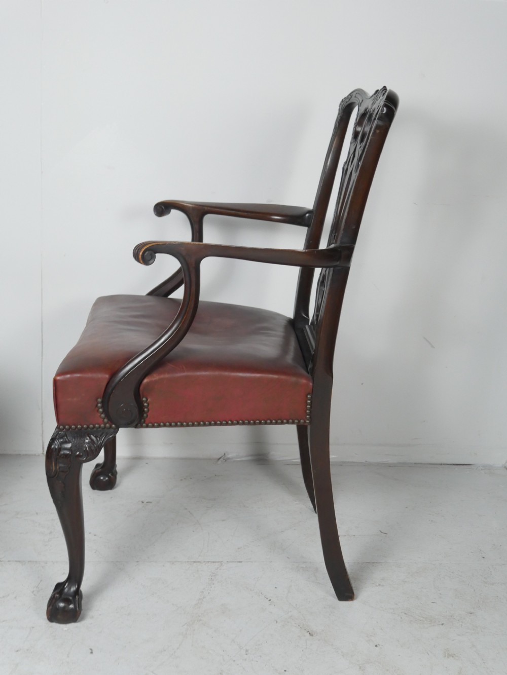 A pair of 19th-century Chippendale style mahogany armchairs featuring pierced back splats, reddish-brown leather seats with studding, and cabriole legs with ball-and-claw feet. View X