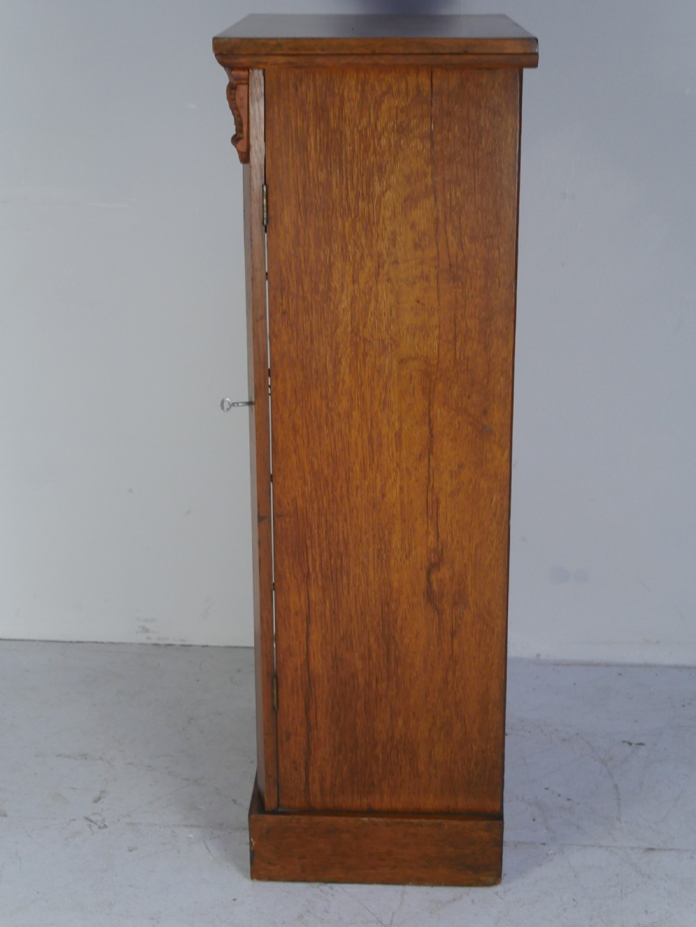 A tall Victorian oak Wellington chest featuring seven drawers with turned wooden knob handles, carved corbels at the top corners, and a locking side flap. View VI