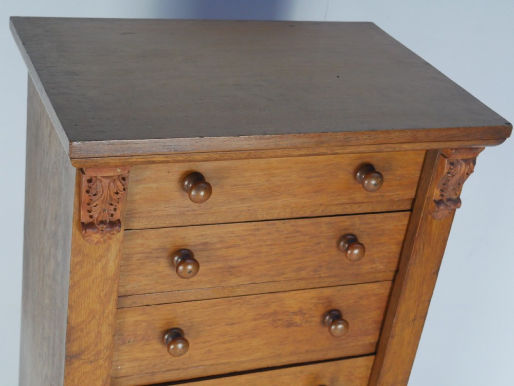 A tall Victorian oak Wellington chest featuring seven drawers with turned wooden knob handles, carved corbels at the top corners, and a locking side flap. View IX