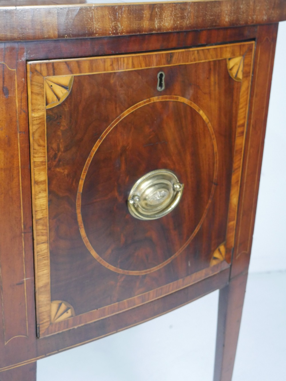 A Georgian bow-front mahogany sideboard featuring satinwood inlays, brass oval handles, and square tapered legs. View III