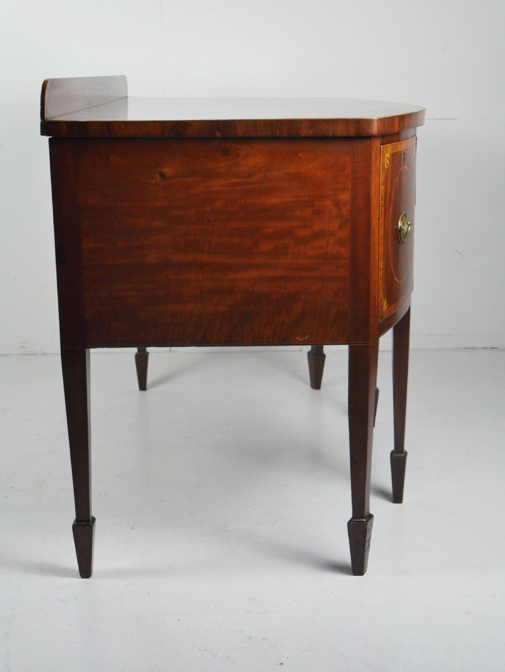 A Georgian bow-front mahogany sideboard featuring satinwood inlays, brass oval handles, and square tapered legs. View VI