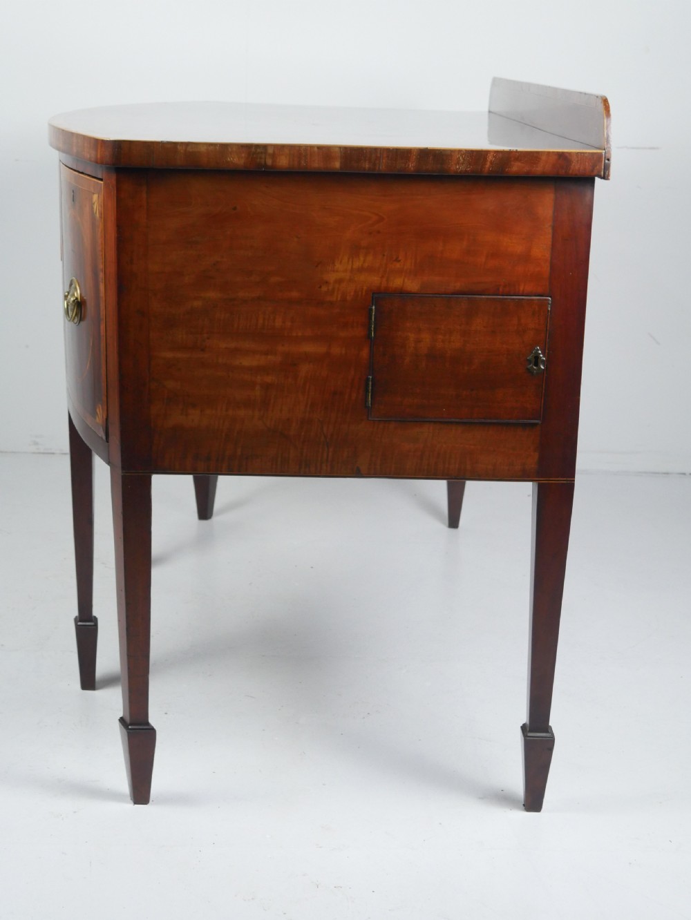 A Georgian bow-front mahogany sideboard featuring satinwood inlays, brass oval handles, and square tapered legs. View VII